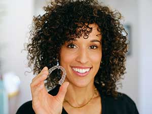 A young woman smiling, holding her clear aligner tray.